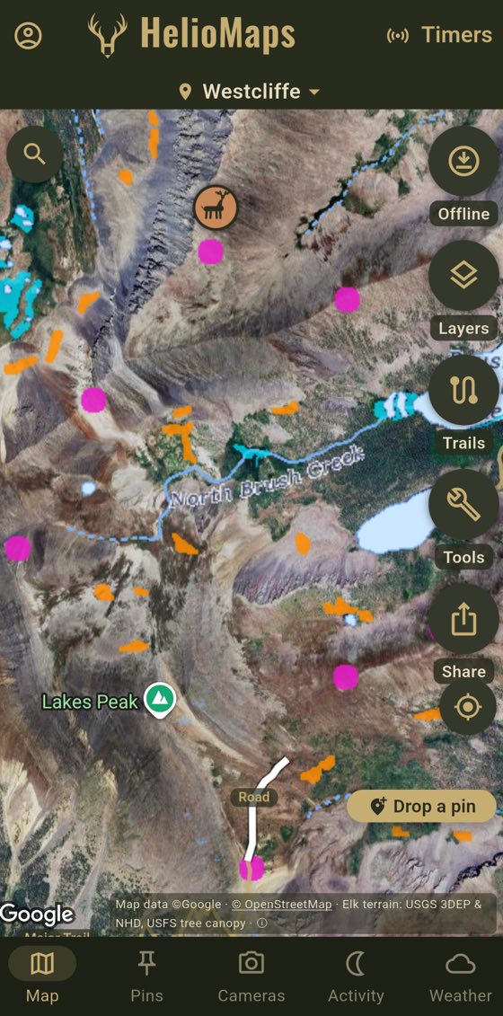 The HelioMaps map over satellite imagery of steep mountain ground with timber, a creek and a lake, an elk pin near the top, and the marks of the elk terrain finder layer. The credit line reads Elk terrain: USGS 3DEP & NHD, USFS tree canopy.